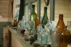 A collection of many glass bottles of various sizes, looking old and dusty